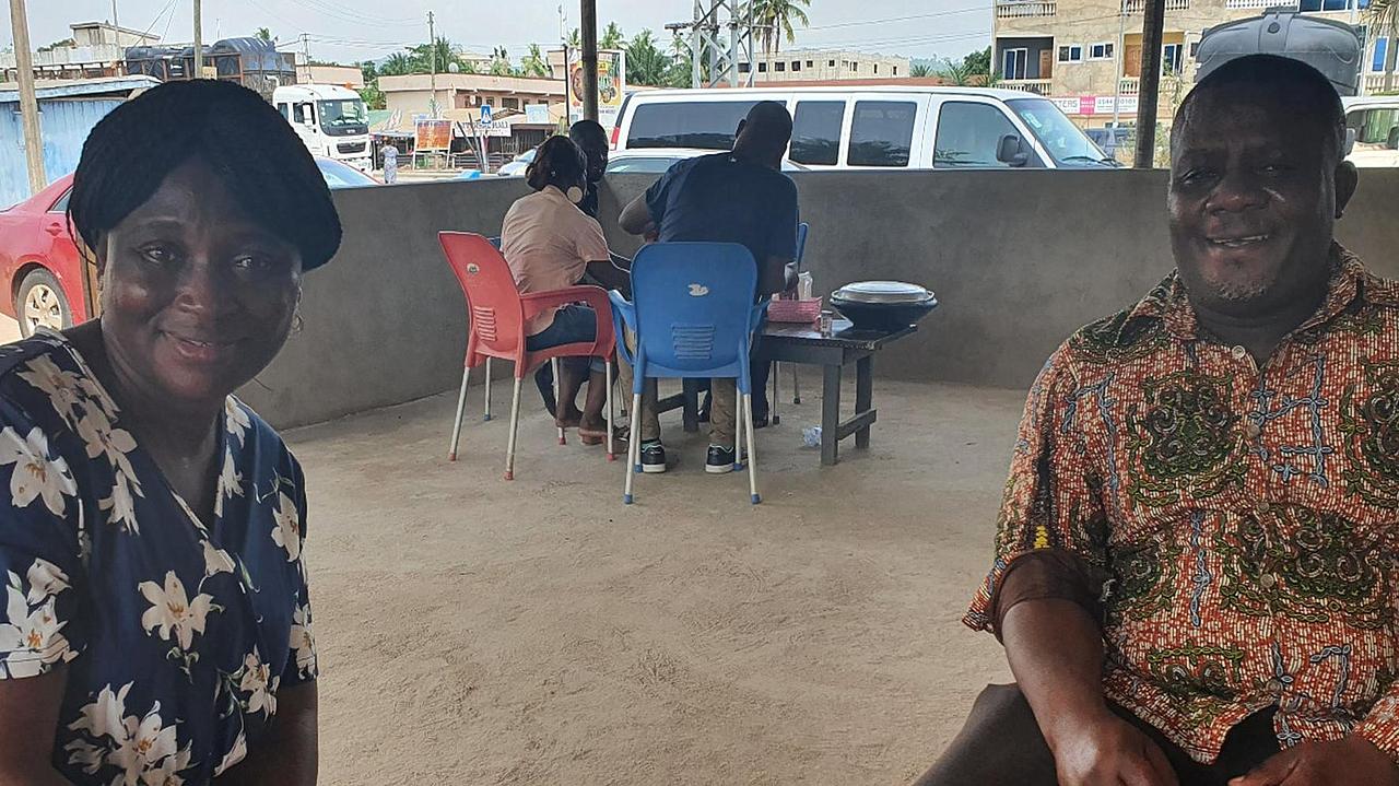 Mehrere ghanaische Personen sitzen im Außenbereich eines Restaurants an zwei Tischen beim Essen.
